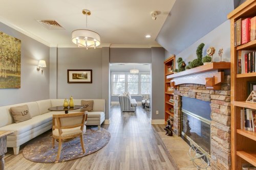 Cozy living room with a stone fireplace, modern furniture, and large windows, featuring a circular table and decorative plants.