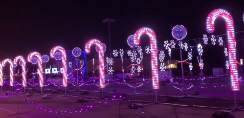 Colorful holiday lights shaped like candy canes and snowflakes illuminate a nighttime scene.