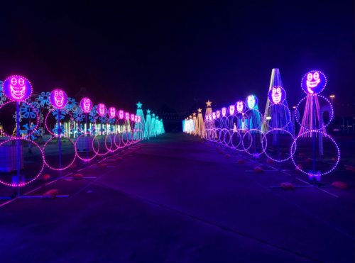 Colorful illuminated figures with smiling faces line a pathway at night, creating a festive atmosphere.