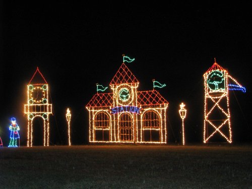 Colorful holiday lights form a festive scene with a clock tower, a building, and a tower, all against a dark night sky.