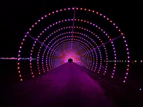A vibrant tunnel of colorful lights in purple and pink, creating a mesmerizing visual effect against a dark background.