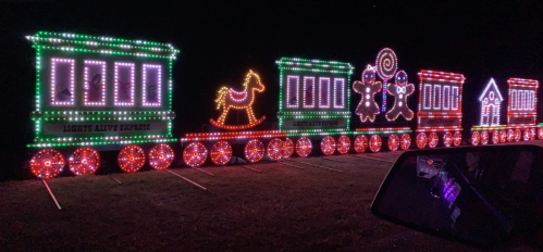 A brightly lit train made of colorful holiday lights, featuring a horse, candy, and festive decorations at night.