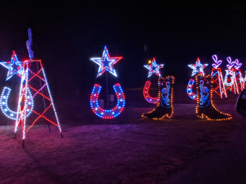 Colorful holiday lights in the shape of stars, horseshoes, and cowboy boots, illuminating a dark outdoor scene.