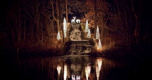 A serene night scene featuring a waterfall illuminated by festive lights and decorated trees, reflecting in the water.