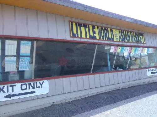 Exterior of "Little World Asian Market" with large signage, windows displaying menus, and an "Exit Only" sign.