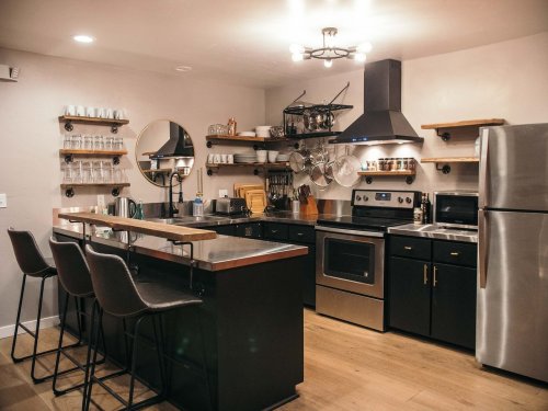 Modern kitchen with black cabinets, stainless steel appliances, a large island with bar stools, and open shelving.