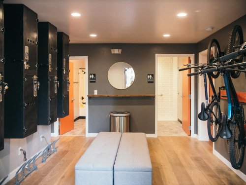 A modern locker room with black lockers, a round mirror, a bench, and bikes mounted on the wall.