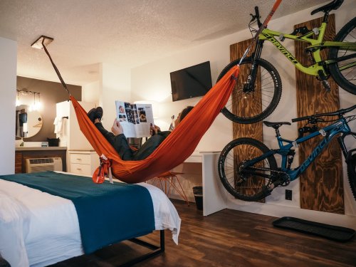 A person relaxes in a hammock in a stylish room with bikes mounted on the wall and a magazine in hand.