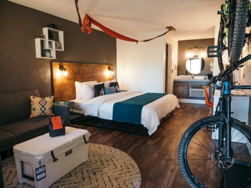 Cozy hotel room with a bed, seating area, bike, and hammock, featuring modern decor and warm lighting.