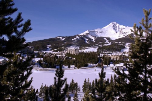 Snow-covered mountains rise above a winter landscape, with a small town nestled among evergreen trees.
