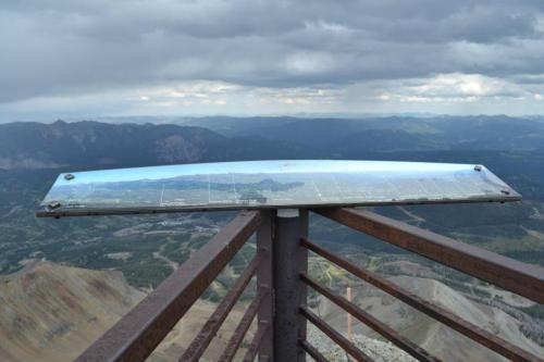 Viewpoint with a metal observation panel overlooking a mountainous landscape under a cloudy sky.