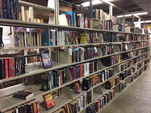 A spacious library shelf filled with a variety of books in different genres, neatly organized on multiple levels.