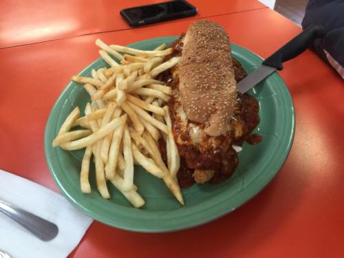 A plate with a large sandwich topped with sauce and a side of golden French fries on a bright orange table.