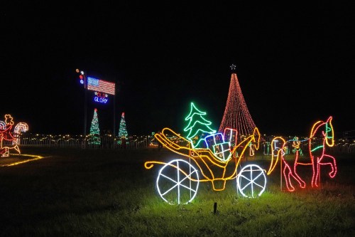 Colorful holiday lights display featuring a decorated carriage, trees, and a tall Christmas tree against a night sky.
