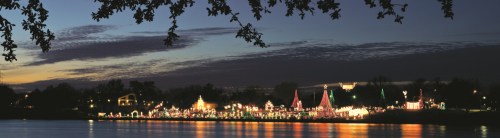 A serene evening scene of a lake adorned with colorful holiday lights and decorations, reflecting on the water.