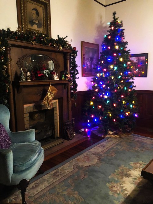 A cozy room with a decorated Christmas tree, a fireplace adorned with garlands, and a blue armchair.