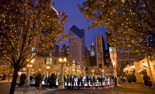 A bustling ice skating rink surrounded by twinkling lights and skyscrapers at dusk.