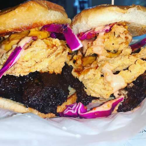 A close-up of a sandwich with fried chicken, coleslaw, and sauce between two toasted buns.