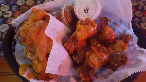 A basket of crispy chicken wings with a side of dipping sauce, served on parchment paper.