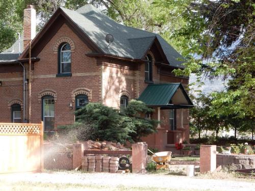 A brick house with a green roof, surrounded by trees and a garden, featuring a wheelbarrow and flower beds in the yard.