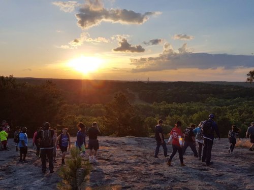 A group of people hiking on a rocky terrain at sunset, with a lush green landscape in the background.