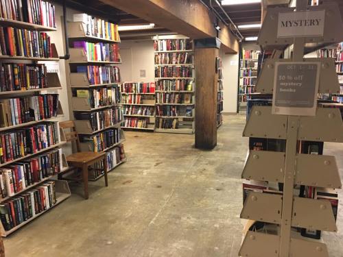 A cozy bookstore aisle filled with shelves of books, featuring a sign for 50% off mystery books.