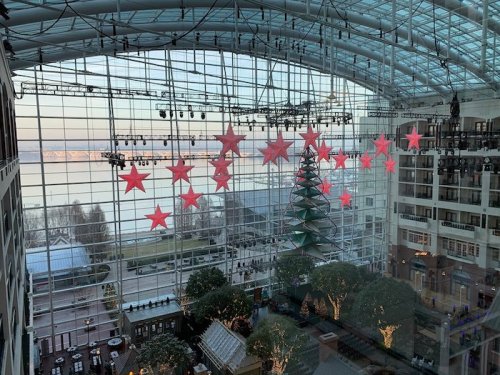 A festive indoor space with large red stars and a Christmas tree, featuring a glass ceiling and scenic views outside.