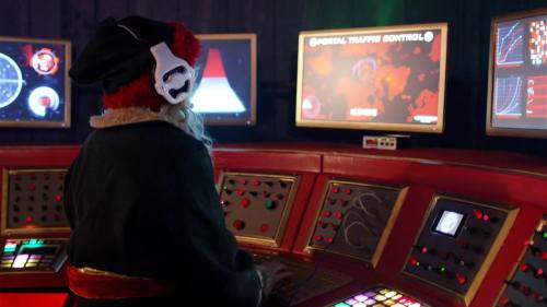 A figure in a Santa costume operates a high-tech control panel with multiple screens and colorful buttons.
