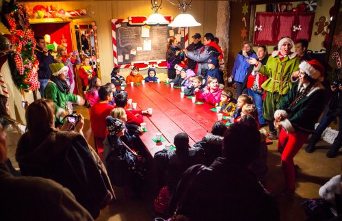 A festive gathering with children and adults around a long table, enjoying holiday treats in a decorated room.