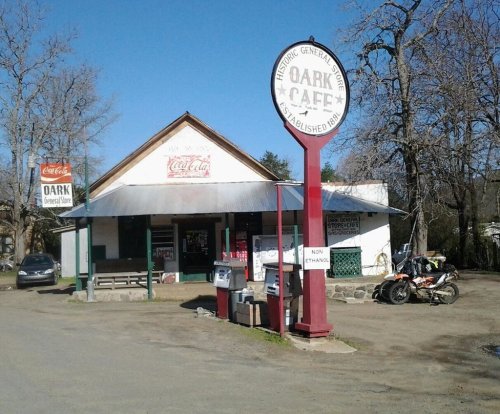Historic general store and café with a sign, surrounded by trees and parked motorcycles.