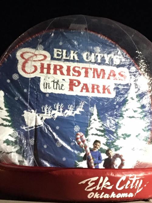 A festive inflatable snow globe with "Elk City Christmas in the Park" and two children posing in front of it.