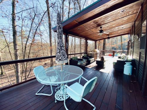 A cozy outdoor deck with a table, chairs, and an umbrella, surrounded by trees and a peaceful natural setting.