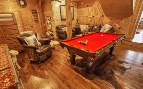 Cozy wooden room featuring a red pool table, leather chairs, and rustic decor.