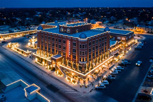 Aerial view of a beautifully lit building at night, surrounded by festive lights and parked cars.