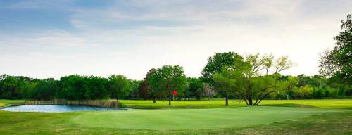 A serene golf course scene featuring a green, a pond, and trees under a clear sky.
