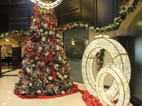 A beautifully decorated Christmas tree with red and silver ornaments next to a large illuminated ornament display.