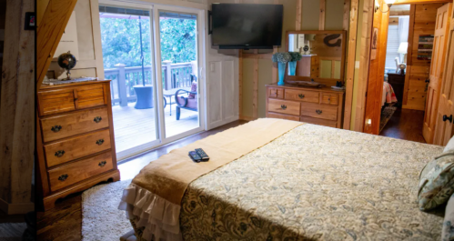 Cozy bedroom with a patterned bedspread, wooden furniture, and a sliding door leading to a deck with outdoor seating.