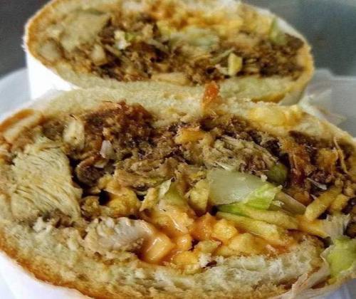 Close-up of a sandwich filled with shredded meat, lettuce, and sauce, served in a soft bread roll.