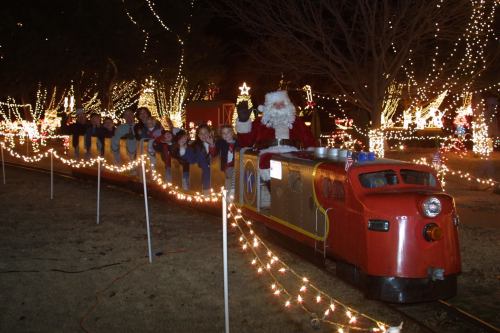 A festive train ride with children and Santa, surrounded by colorful holiday lights in a winter setting.