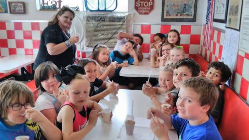 A group of children and an adult enjoy ice cream together at a diner, smiling and posing for the camera.