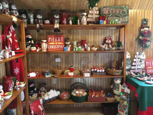 A festive display of Christmas decorations, including snowmen, ornaments, and signs, on wooden shelves.