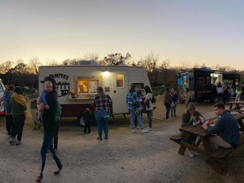 A food truck and coffee trailer serve a crowd at sunset, with people enjoying food and drinks at picnic tables.