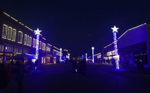 A festive street at night, lined with buildings adorned in blue lights and star-topped decorations.
