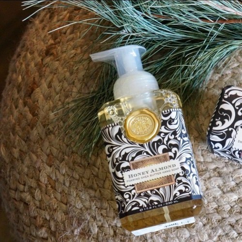 A bottle of honey almond foaming hand soap with a decorative label, placed on a textured surface with greenery.