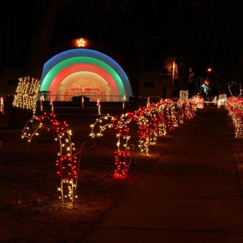Colorful holiday lights illuminate a park, featuring candy cane decorations and a festive arch in the background.