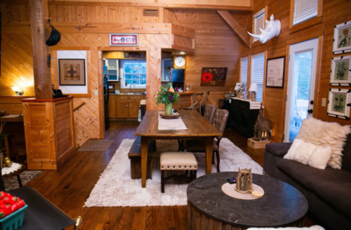 Cozy wooden interior of a cabin with a dining table, living area, and kitchen visible in the background.