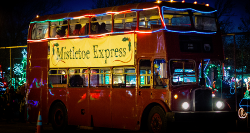 A festive double-decker bus, "Mistletoe Express," adorned with colorful lights, parked in a holiday display.