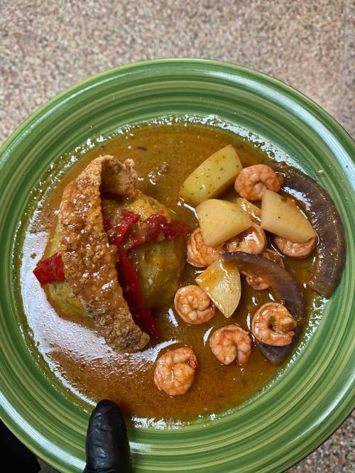 A green plate with shrimp, potatoes, and a piece of fried plantain in a savory sauce.