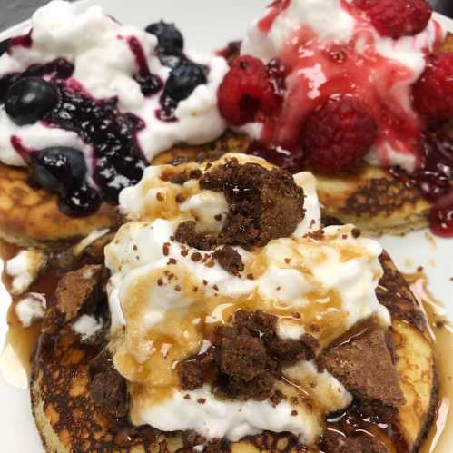 Fluffy pancakes topped with whipped cream, berries, and drizzles of syrup and crushed cookies.