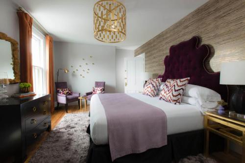 A stylish bedroom featuring a purple headboard, gold accents, and cozy seating by the window.